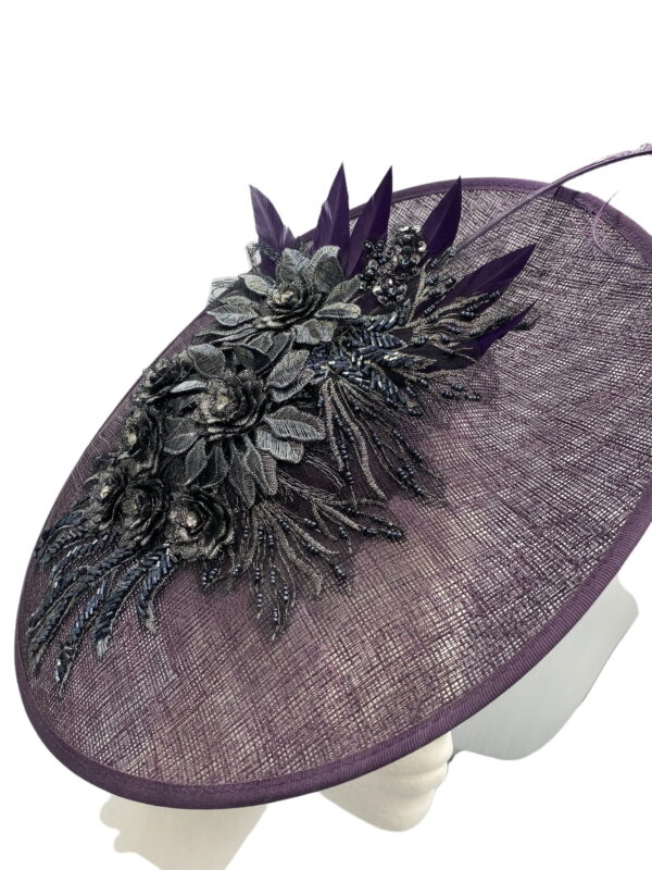 Purple saucer style headpiece with pewter embellishment to the side finished with a spray of colour matching feathers.